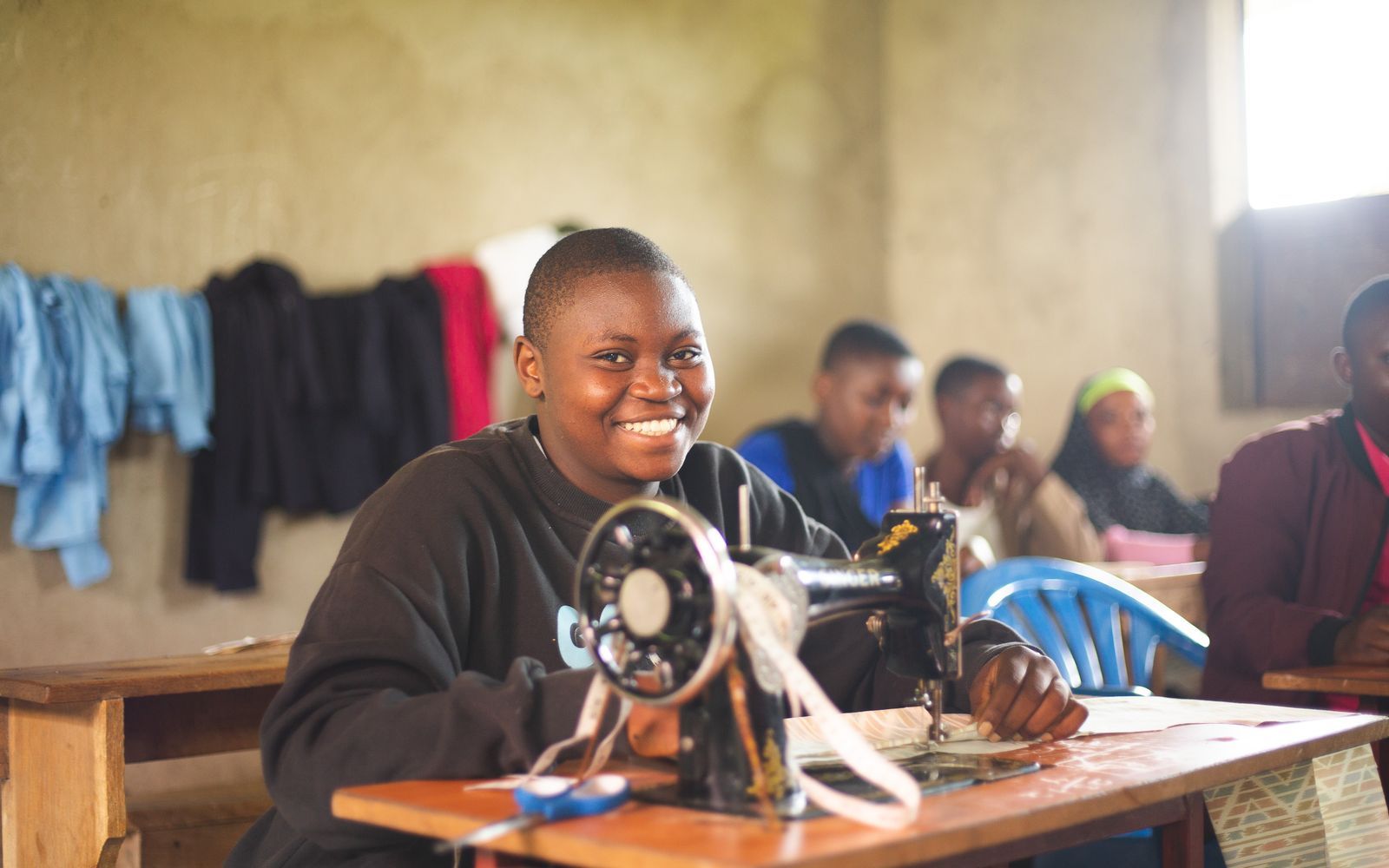 Apprenante souriante à sa machine à coudre pendant un atelier de formation professionnelle